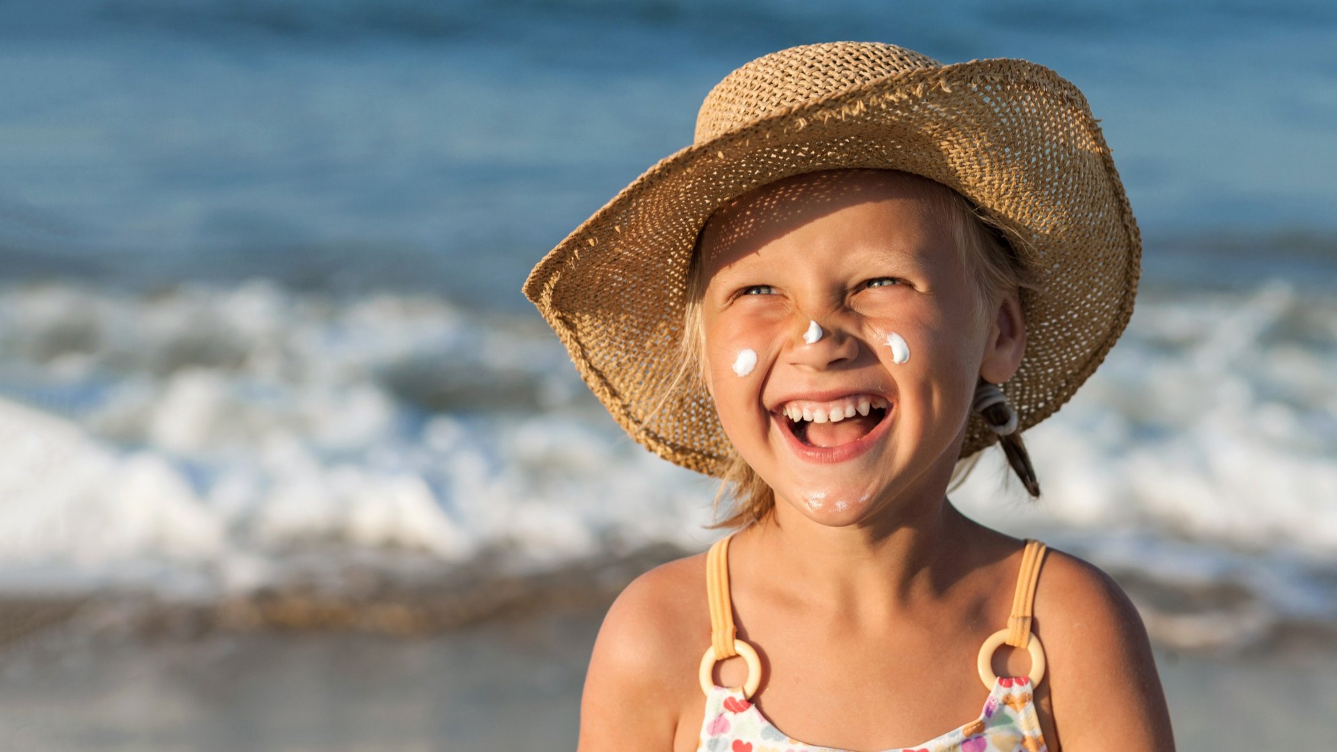 Smiling child with hat and sunscreen at the beach.